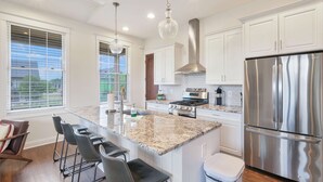 A kitchen with white cabinets, a stainless steel refrigerator, a gas stove, and a bar area with stools.
