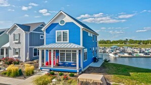 A blue house with a porch, a garage, and a view of a marina with boats. - Striking Waterfront Villa Home (Ottawa)