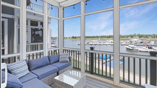 A covered outdoor deck with a sofa and table, overlooking a marina with boats. - Striking Waterfront Villa Home (Ottawa)