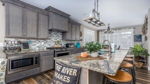 A modern kitchen with granite countertops, dark cabinetry, and a central island with bar stools. - Striking Waterfront Villa Home (Ottawa)