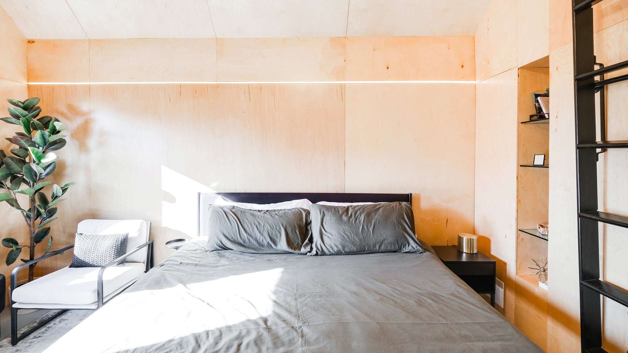 A modern bedroom with a bed, a bedside table, a chair, and a plant.