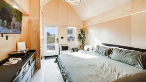 A bedroom with a bed, a desk with a computer, a chair, a plant, and a door leading outside. - The Bunkies @ Heritage Harbor (Ottawa)