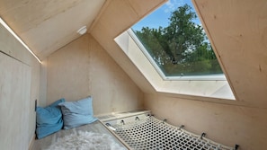 Ein Zimmer mit schrägem Dach, einem Oberlicht, einer Hängematte und einem Bett mit Kissen.