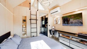 Een slaapkamer met een bed, een bureau, een stoel, een televisie en een kitchenette.