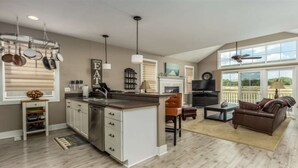 Een ruime keuken met een groot eiland, een eetgedeelte met een bruine leren bank en een woonkamer met een televisie en een open haard.