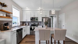 A modern kitchen with white cabinets, stainless steel appliances, and a bar area with two chairs. - Dog Friendly Condo | Navvy Town Neighborhood (Ottawa)