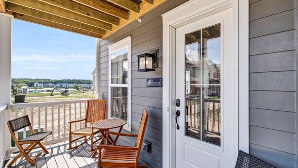 A covered porch with wooden furniture, a door with a keypad, and a view of a beach and houses. - Dog Friendly Condo | Navvy Town Neighborhood (Ottawa)
