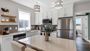 A modern kitchen with white cabinetry, stainless steel appliances, a central island, and pendant lighting.