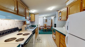 A compact kitchen with wooden cabinets, a white stove, and a dining area with a green carpet.