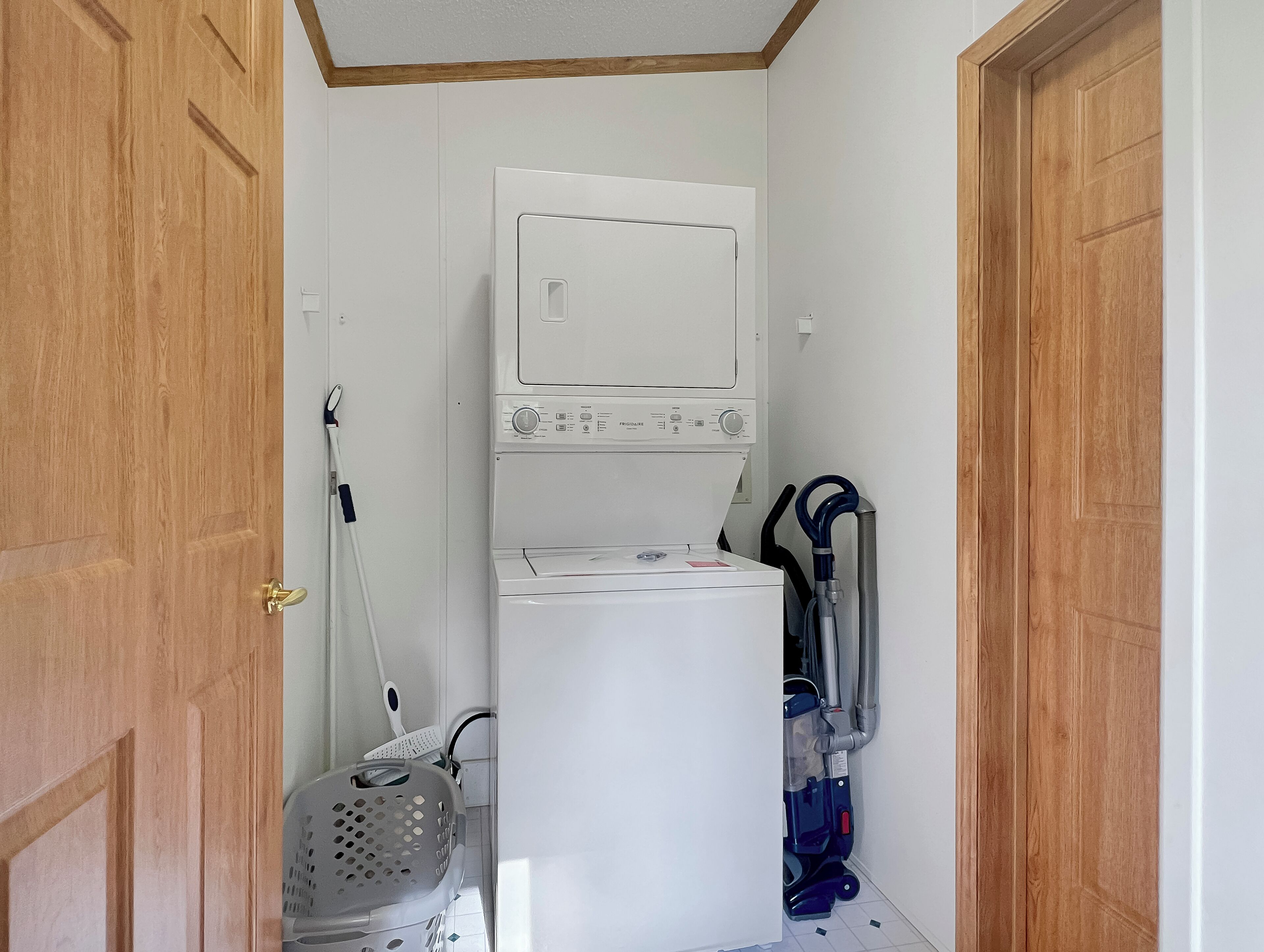 Une buanderie équipée d’un lave-linge et d’un sèche-linge superposés, d’un panier à linge et d’un aspirateur.