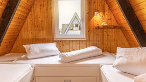 Een knus slaapkamer onder het dak met twee bedden, een raam met uitzicht op een huis en een bedlampje.