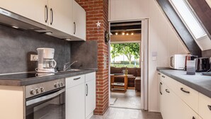 Een kleine keuken met een koffiezetapparaat, fornuis en uitzicht op een eethoek met een bank en tafel.