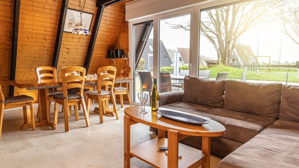 Een gezellige kamer met een houten eettafel en stoelen, een bank en een groot raam met uitzicht op de omgeving.