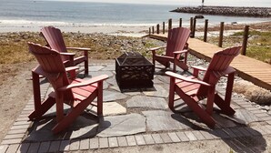 A beachside seating area with red Adirondack chairs and a black fire pit, overlooking the ocean.