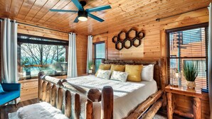 A log cabin bedroom with a wooden bed, a ceiling fan, and a view of the outdoors.