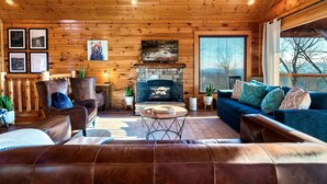 A cozy cabin interior with a stone fireplace, leather sofas, and wooden walls.