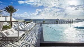 A rooftop infinity pool with lounge chairs and a palm tree.