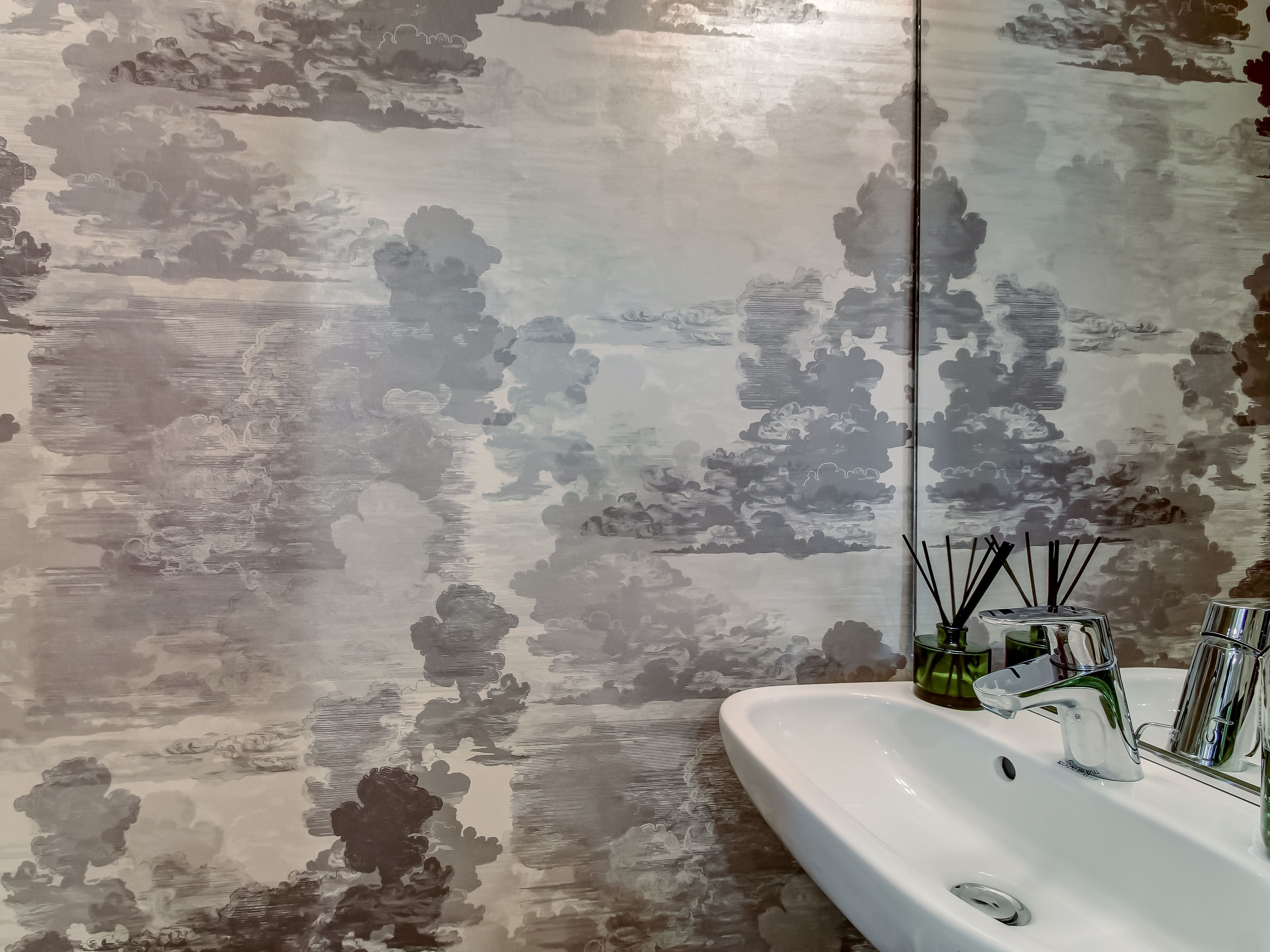 A bathroom with a white sink, a mirror, and a wall with a cloud pattern design.