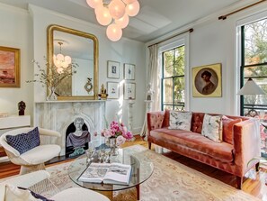 A well-lit living room with a fireplace, a sofa, a coffee table with a book, and a large mirror.