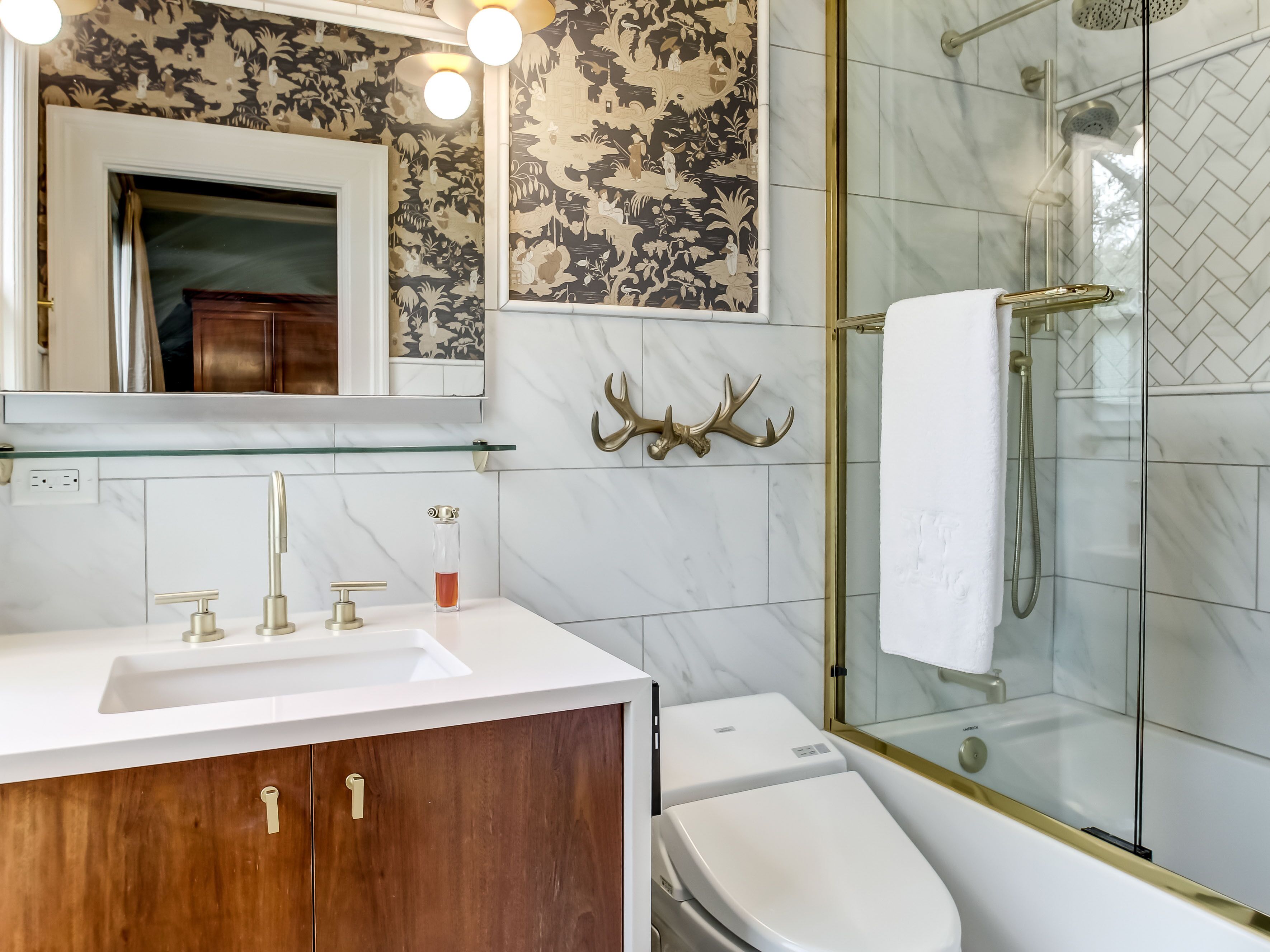 Une salle de bain avec un lavabo blanc, des robinets dorés, un distributeur de savon en verre, des toilettes et une cabine de douche en verre.