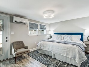 Une chambre à coucher comprenant un lit, une chaise, une fenêtre avec des rideaux à motifs, un appareil de climatisation et un tapis à motifs.