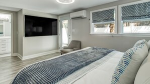 Ein modernes Schlafzimmer mit einem großen Bett, einem an der Wand montierten Fernseher und einem Fenster mit gemusterten Vorhängen.