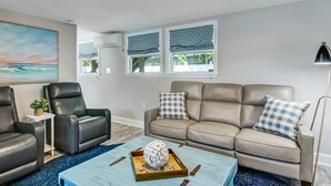 Ein modernes Wohnzimmer mit einem beigefarbenen Sofa, zwei schwarzen Ledersesseln, einem blauen Couchtisch mit einem dekorativen Gegenstand und einer Deckenleuchte.