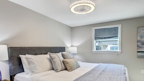 Un dormitorio con cama, mesitas de noche, una ventana con cortinas estampadas y una lámpara en el techo.