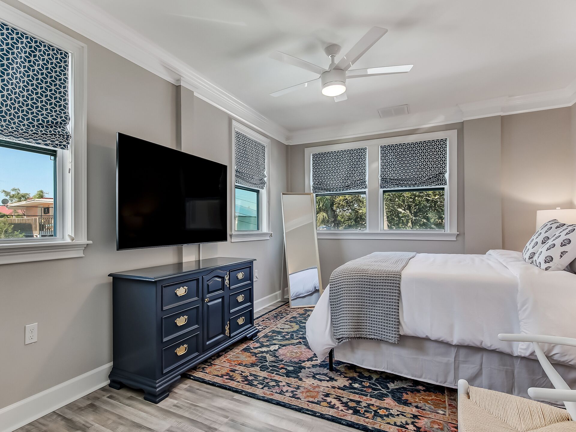 A bedroom with a bed, a TV, a dresser, and a ceiling fan.