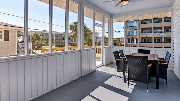 Eine überdachte Terrasse mit Tisch und Stühlen, großen Fenstern und einem Deckenventilator.