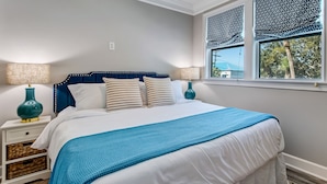 Ein Schlafzimmer mit einem Bett, zwei Nachttischen, einem Deckenventilator und einem Fenster mit verzierten Fensterläden.