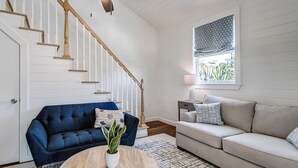 A living room with a blue sofa, a beige sofa, a wooden coffee table, a ceiling fan, and a window with patterned curtains.