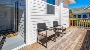 A covered deck with a wooden floor, two chairs, and a table.