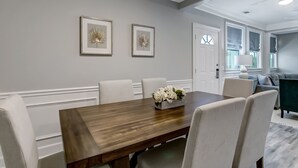 A dining area with a wooden table, white chairs, and two framed wall art pieces. - Multi-Unit Home, Steps to the Beach, Pool Access (Tybee Island)