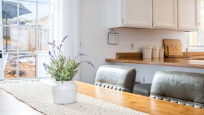 A dining area with a wooden table, white chairs, a white vase with lavender, and white cabinets. - Mulberry Dreams+Stocked Kitchen+Backyard+Wineries (Templeton)