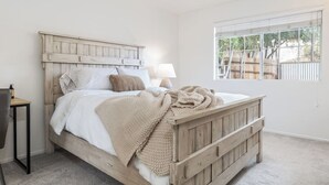 A bedroom with a wooden bed, white bedding, a bedside lamp, and a window with a view of trees. - Mulberry Dreams+Stocked Kitchen+Backyard+Wineries (Templeton)