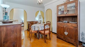 Una zona de menjador amb taula de fusta, cadires, un armari amb portes de vidre i una làmpada penjant.