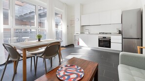 A modern kitchen with white cabinets, a stainless steel refrigerator, and a dining area with a table and chairs. - GuestHost - Industrial Design Apt near M4 Tolstoy (Milano)