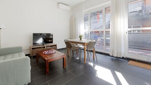 A modern living room with a flat-screen TV, a sofa, a dining table with chairs, and large windows with curtains. - GuestHost - Industrial Design Apt near M4 Tolstoy (Milano)