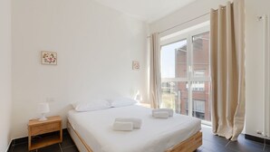 A bedroom with a bed, nightstand, and window with curtains. - GuestHost - Industrial Design Apt near M4 Tolstoy (Milano)