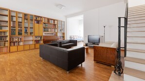Ein modernes Wohnzimmer mit einer Eckcouch, einem Fernseher, einem Holzregal und einer Treppe.