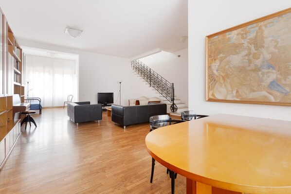 A spacious living room with a wooden floor, a staircase, a large painting, and a dining area with a round table. - GuestHost - Detached house only 550m from Lancetti FS! (Milano)