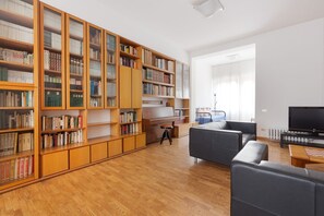 A spacious living room with a large wooden bookshelf, a piano, a sofa, and a television. - GuestHost - Detached house only 550m from Lancetti FS! (Milano)