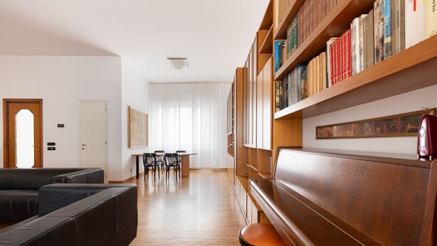 Ein modernes Wohnzimmer mit einem Ecksofa, einem Holzregal und einem Essbereich mit Stühlen und einem Tisch.