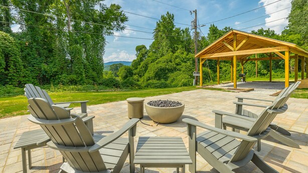 Un patio al aire libre con sillas Adirondack, un brasero y un pabellón de madera.