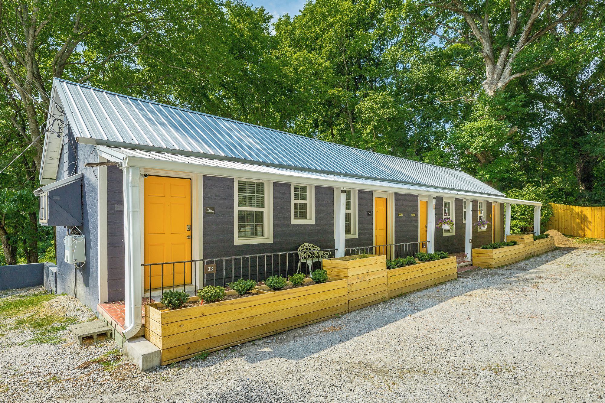 A single-story building with a metal roof, a yellow door, and a small porch area with wooden planters.