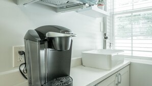 Una cafetera sobre una encimera blanca en una cocina moderna con ventana y armarios blancos.