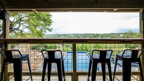 Une terrasse en bois avec trois tabourets de bar en métal, donnant sur une piscine.