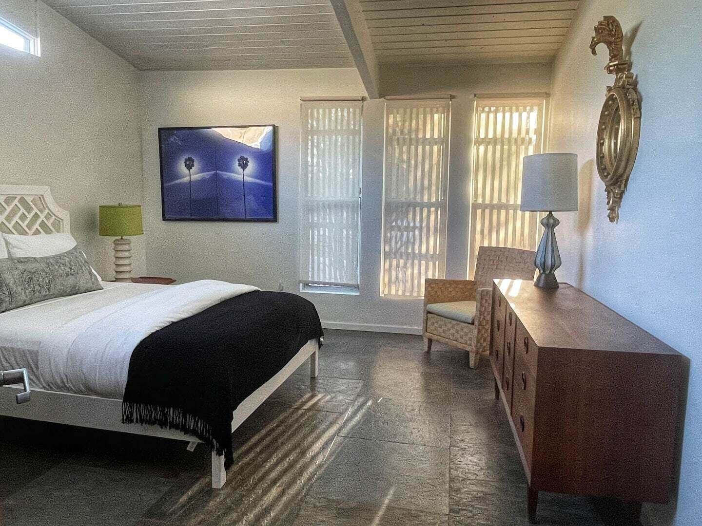 A bedroom with a bed, a chair, a dresser, a painting, and a window with blinds.
