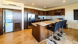 Una cocina moderna con armarios de madera, un refrigerador de acero inoxidable, un horno empotrado y una zona de bar con taburetes.